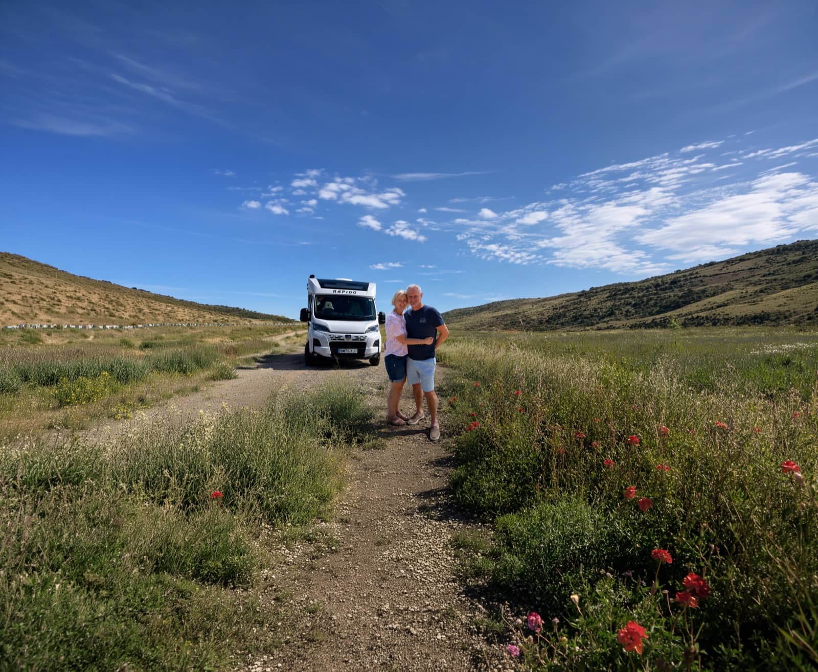 Una coppia in piedi accanto al proprio camper su un sentiero tra verdi colline