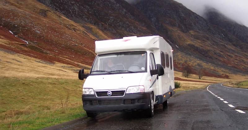 Autocaravan che percorre una strada bagnata tra colline nebbiose