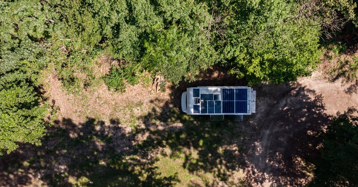Veduta aerea di un camper con pannelli solari sul tetto parcheggiato in una radura della foresta