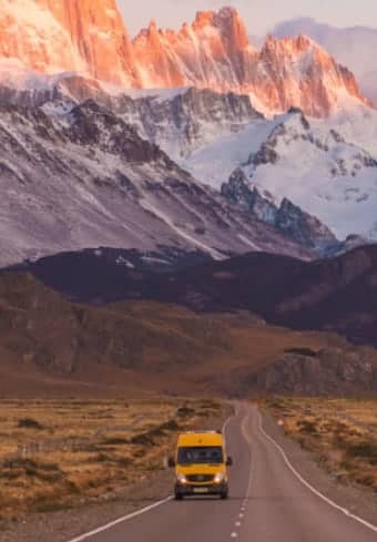 Camper giallo su una strada aperta sotto il massiccio del Fitz Roy coperto di neve in Patagonia